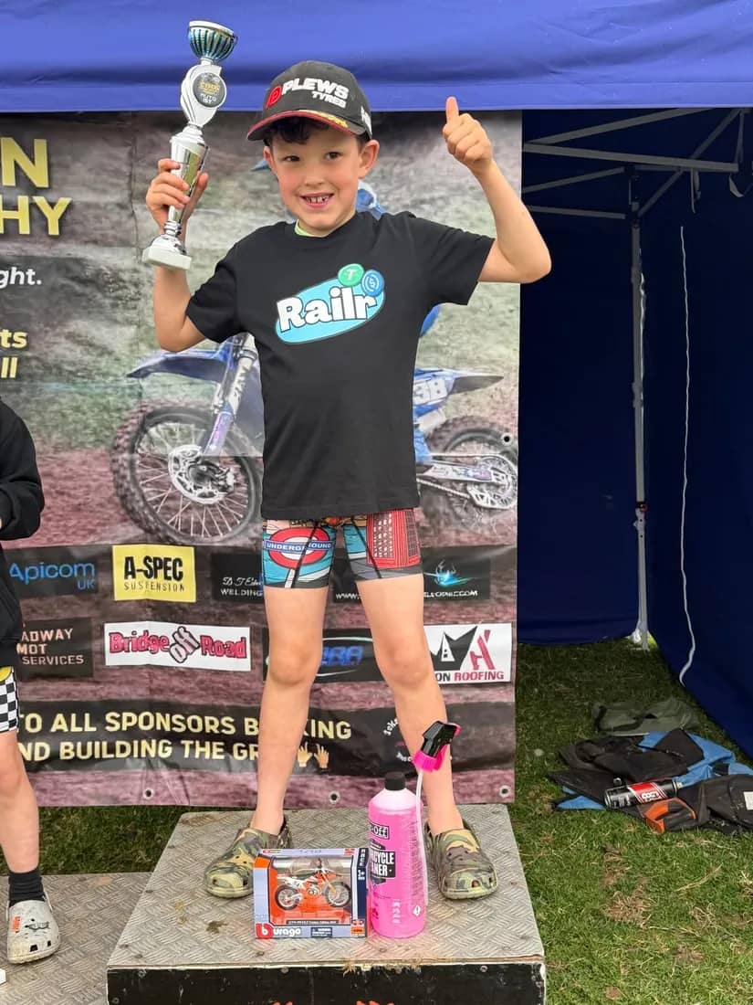 Henry Wilcox on the podium giving a thumbs up with his trophy